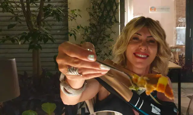 Donna sorridente con un boccone di pizza, in una delle tante rimini restauracje.