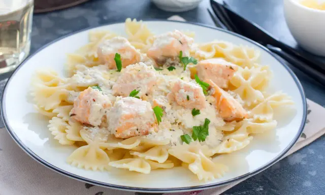 Pyszny makaron farfalle z kawałkami łososia w kremowym sosie, posypany natką pietruszki. Idealny na szybki obiad.