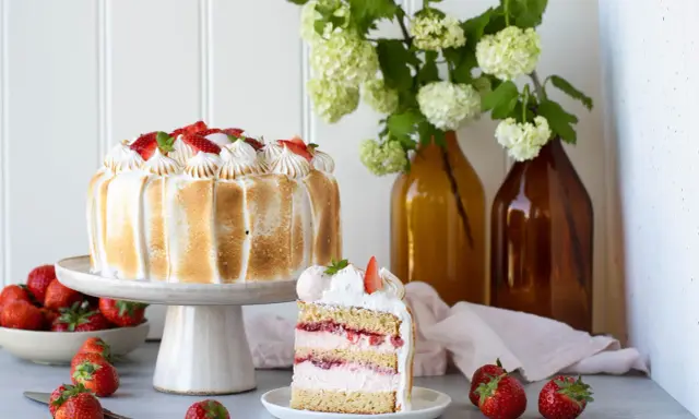 Eine köstliche Erdbeer Baiser Torte mit frischen Erdbeeren und zartem Baiser. Ein Stück der Torte zeigt die saftigen Schichten.
