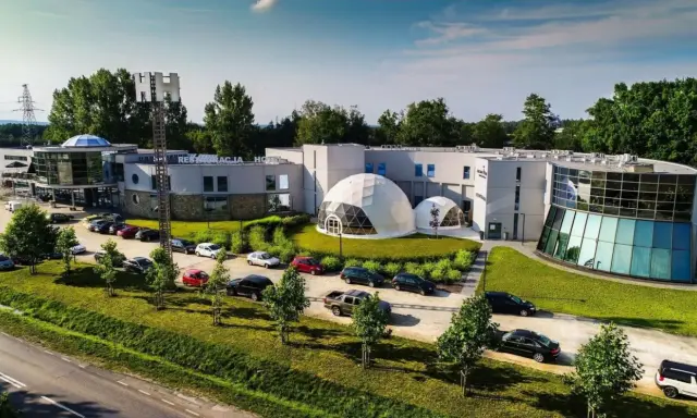 Nowoczesne polskie hotele niezależne z kopułami i przeszklonymi fasadami, otoczone zielenią i parkingiem pełnym samochodów.