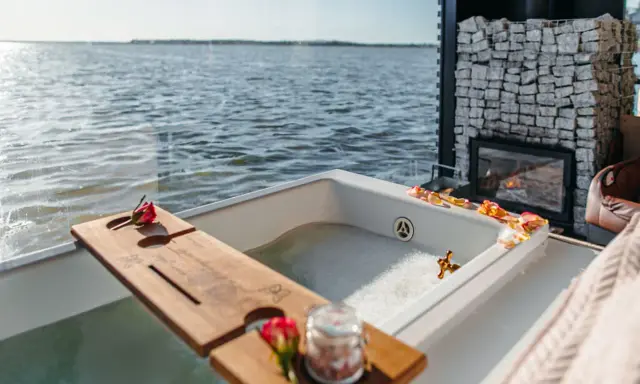 Idealny wypad we dwoje: wanna z pianą i płatkami róż, kominek i widok na wodę.