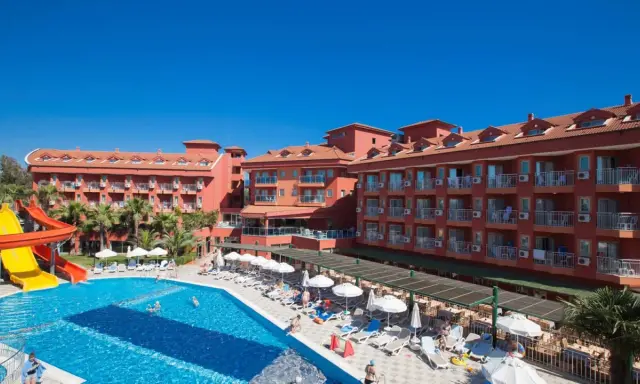 Słoneczny dzień w club side coast. Basen z wodnymi zjeżdżalniami, leżaki i palmy przy hotelu.