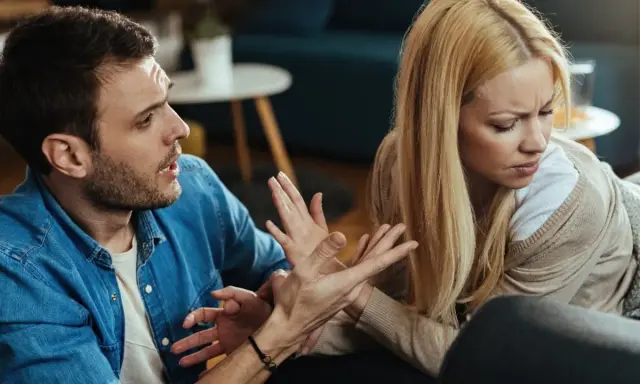 Hombre con expresión de enfado gesticula hacia su pareja, quien lo mira con desprecio, evidenciando una discusión.