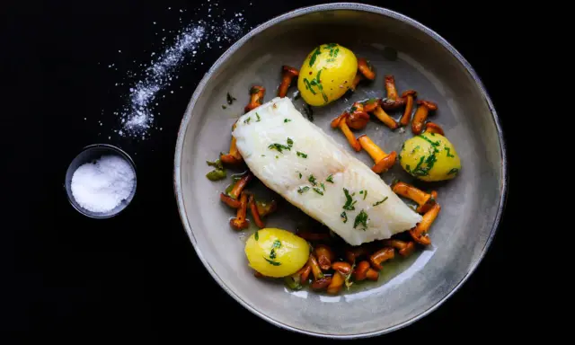 Ein köstliches Heilbutt-Rezept: zartes Fischfilet mit kleinen Kartoffeln und Pfifferlingen, garniert mit frischen Kräutern.