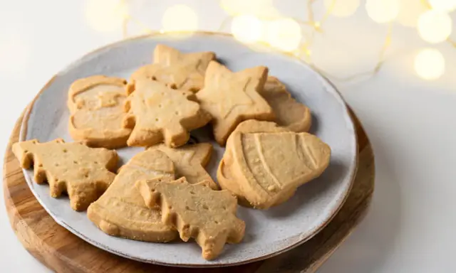 Assortiment de sablés de Noël en forme de sapins, étoiles et cloches, parfaits pour accompagner un chocolat chaud.