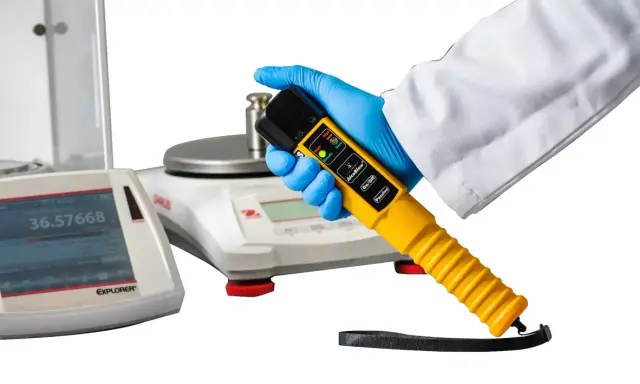 Ręka w rękawiczce trzyma alco sensor 4. Obok wagi laboratoryjne.