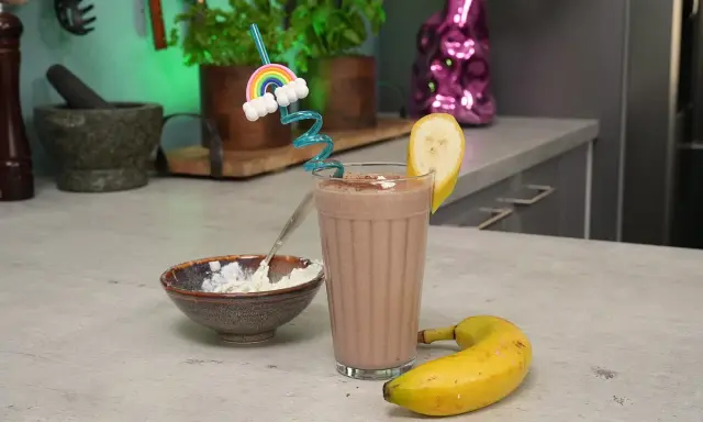 Ein leckerer schoko protein shake mit Banane und einem lustigen Regenbogen-Strohhalm. Daneben eine Schale mit Quark.