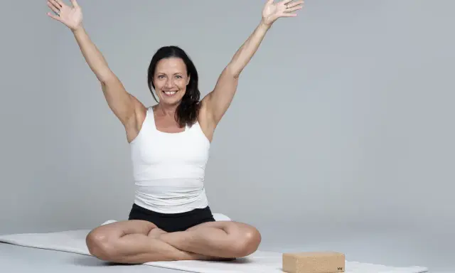 Kvinna i meditationsställning med armarna uppåt, utstrålar lugn och glädje. Hon praktiserar metta meditation för inre frid.