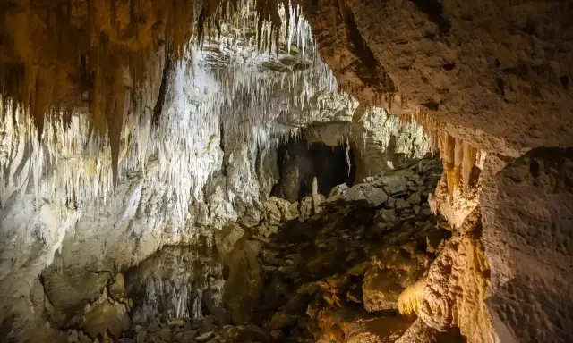 Wnętrze jaskini w Dolinie Kościeliskiej, pełne stalaktytów i stalagmitów. Kamieniste dno i skalne ściany tworzą tajemniczy krajobraz.