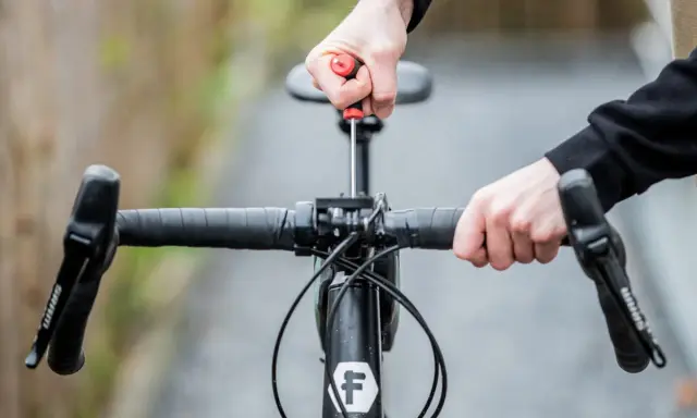 Hände stellen den MTB Lenker ein. Mit einem Schraubenzieher wird die Lenkerposition justiert, um die perfekte Fahrt zu ermöglichen.