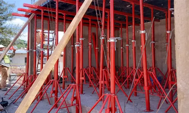 Construcción con varios tipos de puntales rojos sosteniendo una estructura. Un trabajador supervisa.