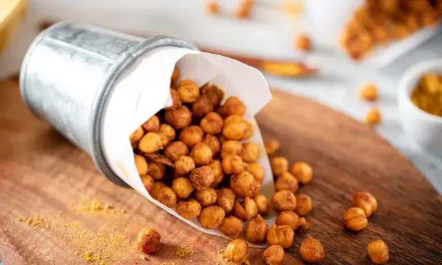 Un seau renversé déverse des pois chiches rôtis, parfaits pour des snacks sains. Une pincée d'épices dorées parsème le bois.
