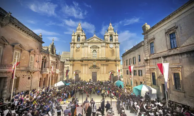 Tłum ludzi w historycznych strojach zgromadzony na placu przed katedrą w Mdina, Malta.