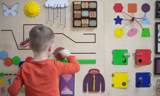 Chłopiec bawi się na tablicy edukacyjnej, rozwijając zdolności manualne. To świetna metoda montessori dla małych odkrywców.
