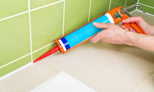 Application de silicone pour maçonnerie sur le joint entre le carrelage mural vert et le plan de travail beige.