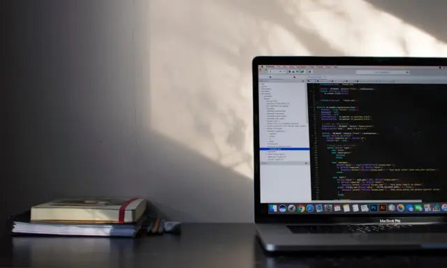Laptop z kodem w języku C#, gdzie pętla `while` jest kluczowa. Obok leżą notatniki i ołówki.