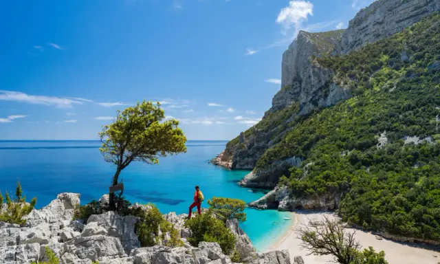 Escursionista ammira una baia cristallina con una spiaggia bianca, incastonata tra imponenti scogliere verdi. Un paesaggio mozzafiato che ricorda la bellezza della montagna centro Italia.