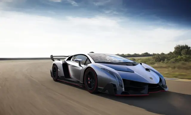 Silberner Lamborghini Veneno Coupé rast auf einer Rennstrecke, die roten Akzente leuchten.