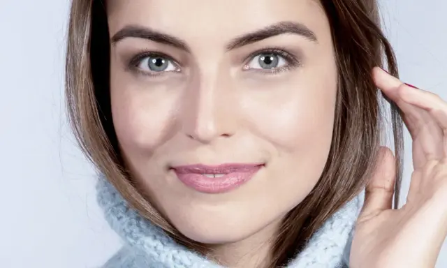 Visage de femme au regard intense, mettant en valeur ses sourcils parfaits. Elle porte un pull bleu ciel.