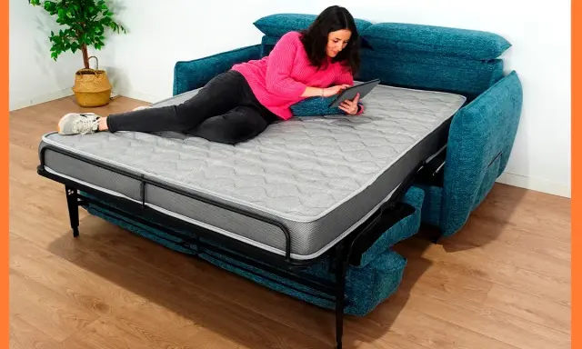 Mujer relajada en un sofá cama abierto, usando su tablet. Los sofabeds son perfectos para ahorrar espacio.