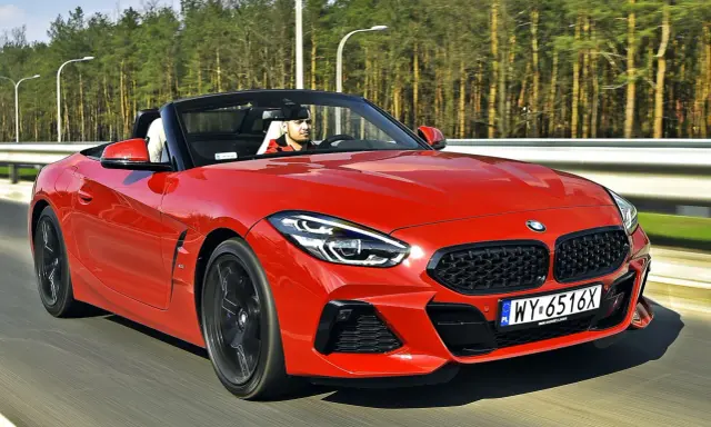 Czerwone z4 bmw z opuszczonym dachem pędzi po drodze, kierowca w czapce z daszkiem cieszy się jazdą.