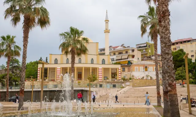 Plac z fontannami i palmami przed meczetem w Durrës, Albania. Ludzie spacerują po schodach.