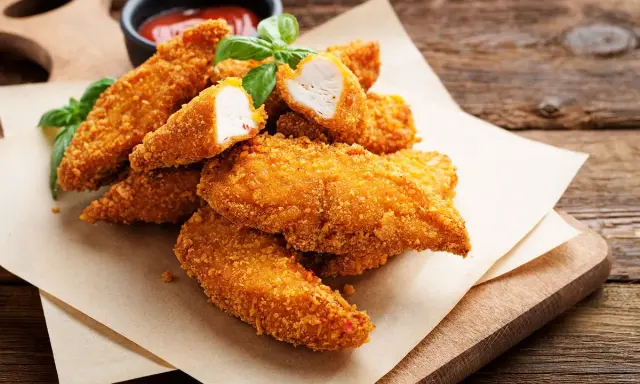 Bocconcini di pollo dorati e croccanti, cotti in friggitrice ad aria, serviti con basilico fresco e salsa.