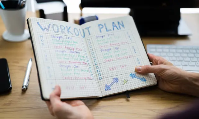 Ein offenes Notizbuch mit einem Trainingsplan, der Übungen und Ruhetage auflistet. Der Plan ist in Spalten für die Tage der Woche unterteilt, mit Kästchen zum Abhaken. Der 3er Split ist klar erkennbar.