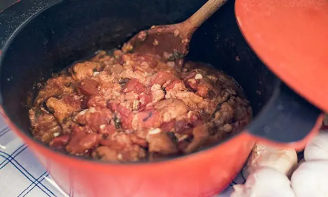 En röd gryta med en mustig toscansk tomatsoppa, en träsked rör om i den väldoftande grytan. Bredvid ligger vitlök.