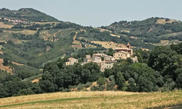Borgo collinare di **Cerreto di Saludecio** con case in pietra e una chiesa, immerso nel verde della campagna romagnola.
