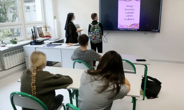 Lekcja religii w szkole. Czy religia wlicza się do średniej? Nauczycielka w habicie i uczniowie patrzą na ekran z informacją o Drodze Krzyżowej.
