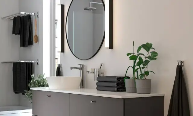 Moderno lavabo con grifería cromada, espejo ovalado y toallas negras. Ideal para una reforma de baño pequeño.