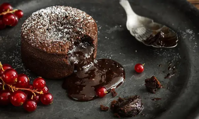 Schokoladen-Lava-Kuchen mit flüssigem Kern, bestäubt mit Puderzucker, garniert mit roten Johannisbeeren. Ein köstliches Lava Cake Rezept.