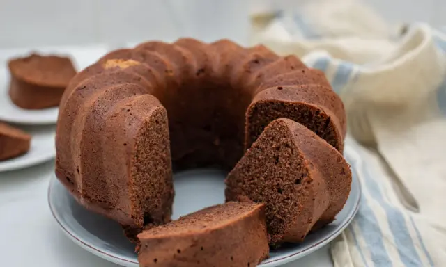 Un soffice ciambellone al cioccolato, appena sfornato, con alcune fette già pronte per essere gustate.