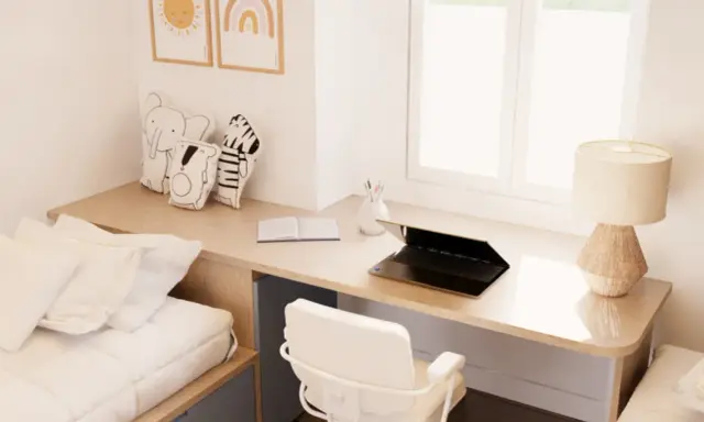 Un escritorio de madera con un portátil, libro y lámpara, junto a una cama y cojines de animales. Este es un ejemplo de cómo un **loft que es** funcional y acogedor.