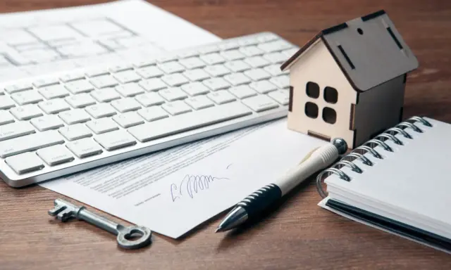 Clé, stylo, maison en bois, clavier et documents sur un bureau. Préparation de la résiliation assurance habitation.