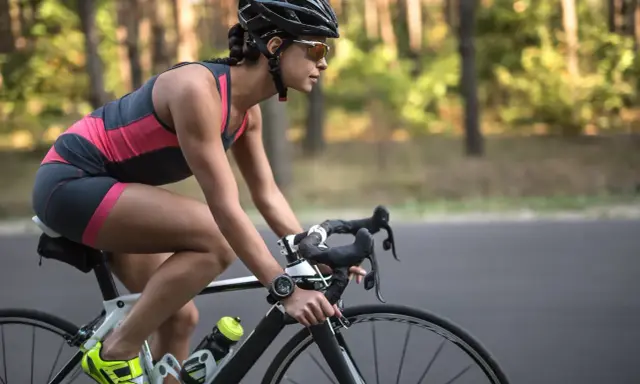 Kobieta w kasku i sportowym stroju podczas jazdy na rowerze. Widać efekty po miesiącu regularnych treningów.