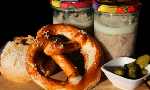 Zwei Gläser mit Fleisch einkochen im Weck-Glas, dazu ein Brezel, Brot und Gewürzgurken.