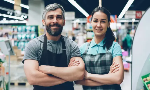 Deux employés souriants, habitués à rester debout toute la journée, posent dans un supermarché.