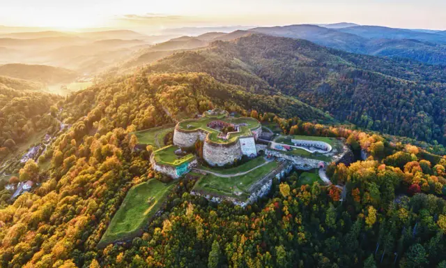 Twierdza na wzgórzu otoczona jesiennym lasem, przypominająca o historii gór blisko Wrocławia.