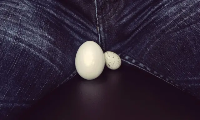 Dwa jajka, jedno duże, drugie małe, leżą na tle dżinsów. Powiększone jądro, symbol płodności.