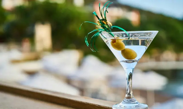 Idealny martini aperitivo z dwiema oliwkami, ozdobiony zielonymi wstążkami, na tle letniego krajobrazu.