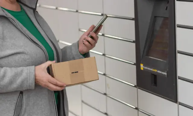Kobieta z telefonem i paczką InPost przy automacie. Weryfikacja paczki InPost przebiega sprawnie.