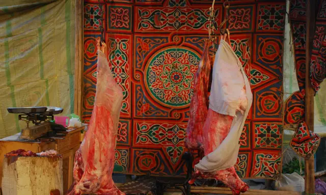 Fleisch hängt vor einem bunten Stoffmuster, bereit für Eid el Adha.