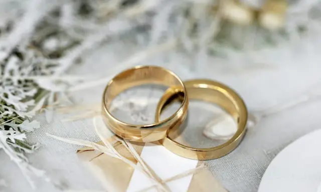 Due fedi dorate intrecciate su uno sfondo delicato. Pensare a cosa incidere sulle fedi è un passo importante per personalizzare questo simbolo d'amore.