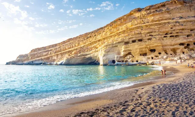 Ein malerischer Strand auf Kreta mit türkisfarbenem Wasser, das sanft an den Kiesstrand schwappt. Die beeindruckende Felswand mit ihren Höhlen bietet eine einzigartige Kulisse.