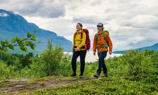 Två glada vandrare med ryggsäckar på en stig i fjällen. En perfekt plats att bo på efter en dag av vandring, kanske på ett STF vandrarhem.