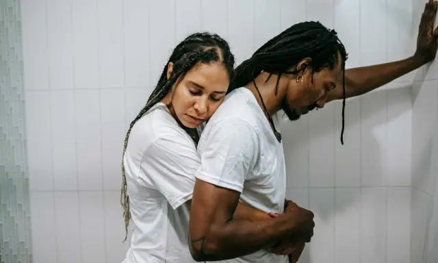 Una pareja se abraza con tristeza, reflejando el momento en que empiezan los problemas de pareja. Él se apoya en la pared, ella recuesta su cabeza en su hombro.