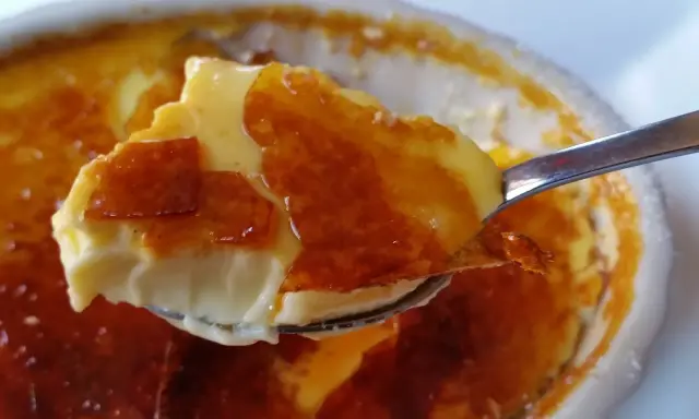 En sked lyfter en bit krämig creme brulee med knäckig karamelliserad yta.