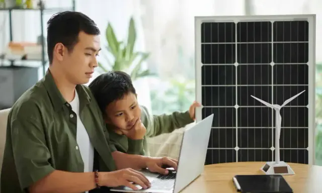 Père et fils étudient l'énergie solaire et éolienne sur un ordinateur portable, un panneau solaire et une éolienne à proximité. Un projet d'installation cacsi sans consuel.